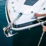 Man s hand with boat rope. Yachtsman moors his motor boat at jetty. Close up hands and bow of the boat.